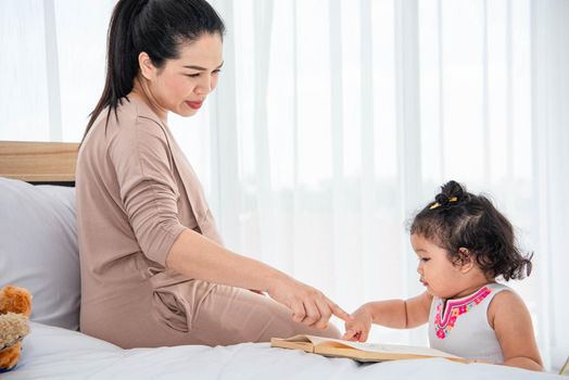 Asian mother teaching girls daughter to reading books in house. Quarantine in home concept. Happy family theme.