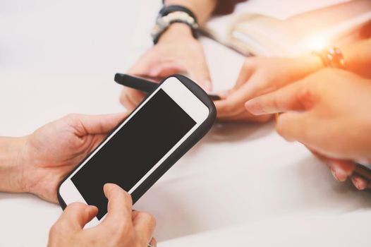 Multiracial friends hand using mobile addicted phone. Wifi connection people on meeting table. Teamwork concept with black blank touch screen phone. Charging and online share information theme.