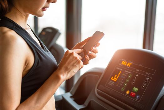 Woman using smart phone when workout or strength training at fitness gym on treadmill. Relax and Technology concept. Sports Exercise and Health care theme. Happy people and Comfortable application