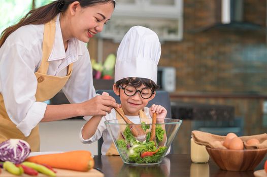 Happy beautiful Asian woman and cute little boy with eyeglasses prepare to cooking in kitchen at home. People lifestyles and Family. Homemade food and ingredients concept. Two Thai people life