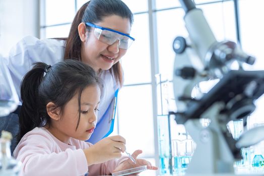 Scientist girl and teacher dropping solution substance liquid with pipette into test tube in lab classroom together. Education and Science. Micro and Nano technology. E-Healthcare and medical concept.