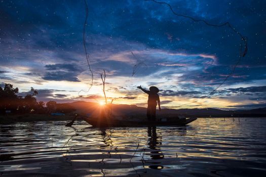 Silhouette Fisherman Fishing by using Net on the boat with sunlight in Thailand , Nature and Culture concept