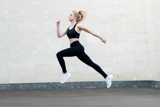 Sport and Fitness Concept Young Adult Caucasian Female Athlete Jumping High Outdoor Gray Tail Wall Background Sportive Woman Jump Exercises Outside Healthy Lifestyle Motivation