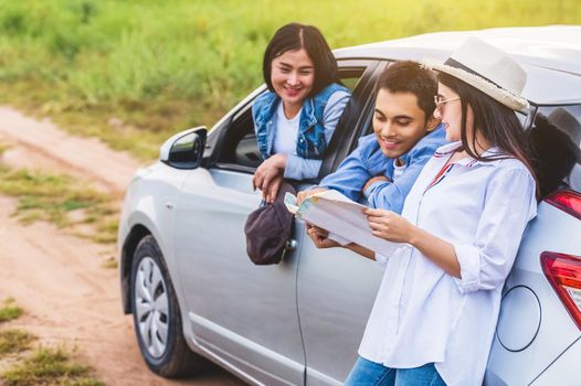 Happy Asian woman and her friends standing by car on coastal road at sunset. Young girl having fun during road trip. People lifestyles and travel vacation concept. Friendship journey and Outdoor tour