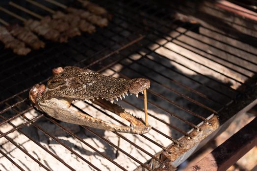 Close up of crocodile head roasted on charcoal stove in street market. Food and exotic cuisine concept.