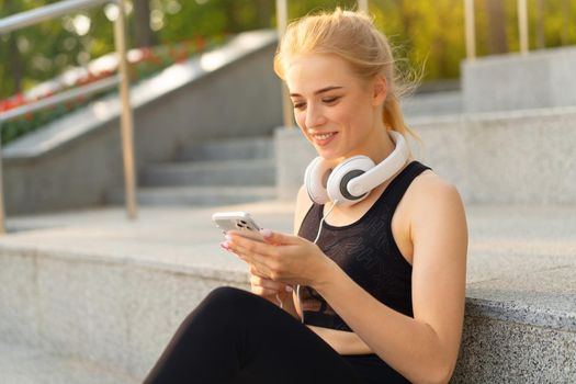 Sport and Fitness Young Adult Caucasian Woman Using Smartphone Concrete Floor Resting after morning Workout Outdoor Summer Park Athletic Female Take a Break Use mobile Phone