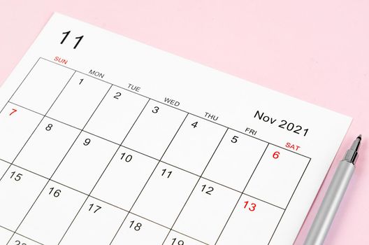 Close up November 2021 calendar sheet with pen on pink background.