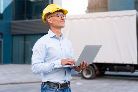 Business. Engineer Worker Protective Helmet Use Laptop Controls Working Process Inspector Supervisor Yellow Hard Hat Glasses Transportation Company Office Building And Truck Background