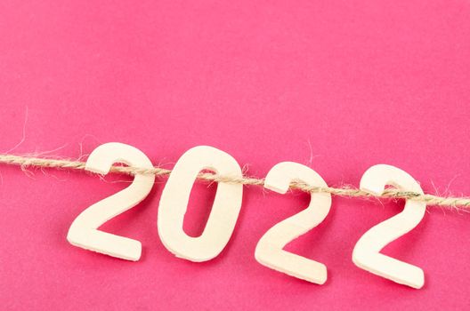 The wooden number 2022 and rope on pink background.