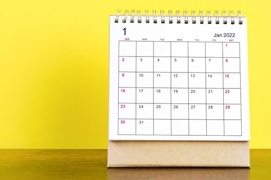 January 2022 desk calendar with yellow background on the wooden table.