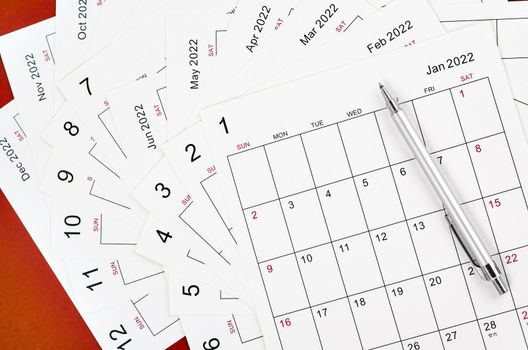 Many blank monthly 2022 calendar sheet with pen on red background.