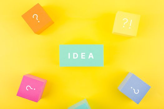 Concept of idea, creativity, start up or brainstorming.Single word idea written on blue rectangle surrounded by multicolored cubes with question signs on yellow background