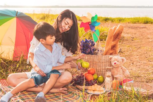 Beautiful Asian mother and son doing picnic and in Easter summer party on meadow near lake and mountain. Holiday and Vacation. People lifestyle and Happy family life concept. Thai person