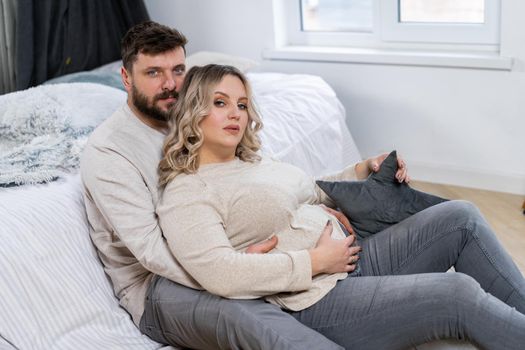 Happy family concept. Husband hug belly pregnant wife sitting floor indoor living room near sofa Caucasian man and woman pregnancy and new life concept. Love and care