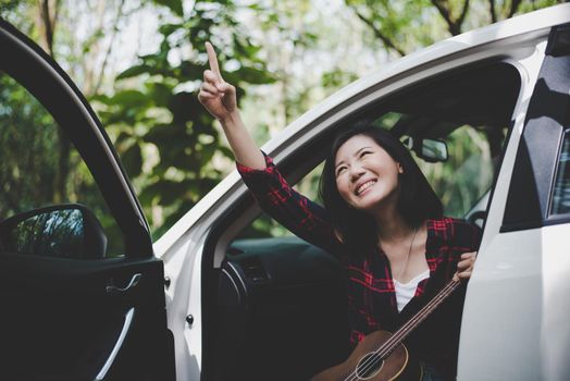 Beauty Asian woman pointing and having fun at outdoors summer with Ukulele in white car. Traveling of photographer concept. Hipster style and Solo woman theme. Lifestyle and Happiness life theme.