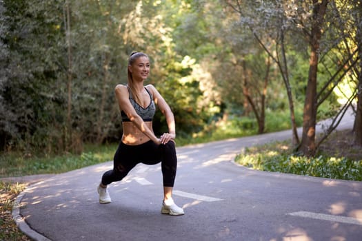Woman runner stretching legs before exercising summer park morning Middle age athletic female warming up body before running Caucasian person warm up jogging running track