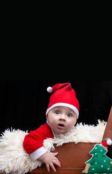 Funny Christmas child in a Santa Claus hat in a retro suitcase on a black background. Kid in Christmas.