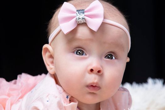 Beautiful baby girl in pink clothes on a black background. Baby at four months old. A funny child.