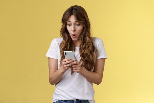 Shocked amazed european girl female blogger become famous online gasping astonished stare camera surprised impressed reading rumors internet social media stand yellow background. Technology concept