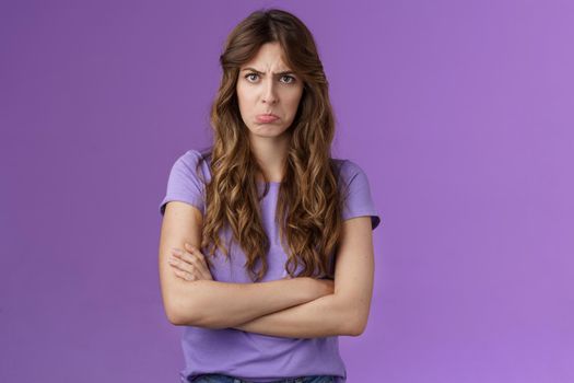 Offended silly timid cute girl sulking pouting lips frowning whining upset cross hands block pose insulted look moody camera disagree acting childish complaining unfair game purple background. Lifestyle.