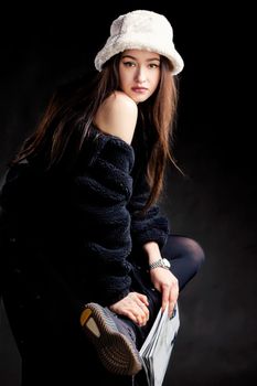 Beautiful stylish girl in dark clothes and a fashionable hat against a dark background.