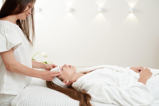 Cosmetologist applying rejuvenating clay facial mask on a female face in beauty salon. Facial treatment concept