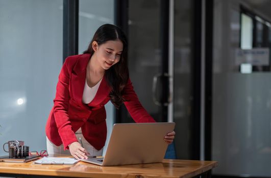 Charming asian woman standing while using laptop computer, female working for financial accounting.