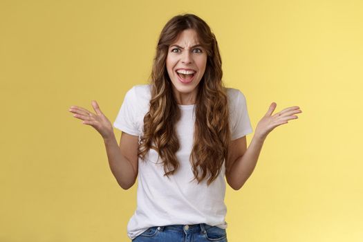 Disappointed angry furious woman shrugging hands sideways dismay frustration shouting complaining feel outraged pissed arguing scream intense rage stand yellow background quarrel.