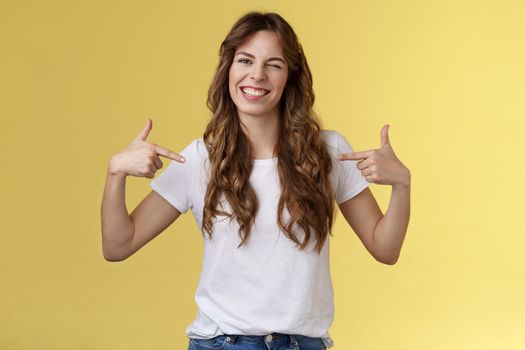 You would not regret this. Sassy good-looking outgoing daring young woman pointing center copy space indicating herself winking joyfully show perfect candidature stand yellow background.