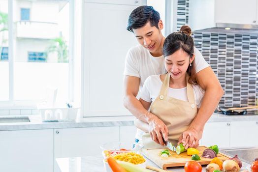 Asian couples cooking and slicing vegetable in kitchen together. Man teaching woman to preparing meal in home. People and lifestyles. Holiday and Honeymoon concept. Valentine day and wedding theme