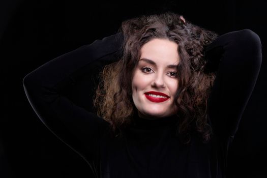 A beautiful brunette girl with curly hair smiles and looks at the camera on a dark background.