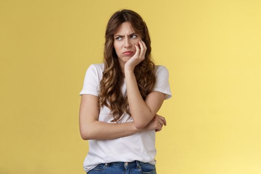 Jealous upset angry moody girlfriend lean palm smirking frowning bothered gloomy look aside turn left dismay sitting lonely offended overthinking drama queen stand yellow background.