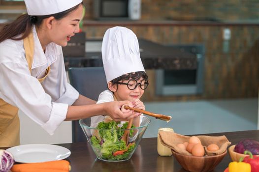 Happy beautiful Asian woman and cute little boy with eyeglasses prepare to cooking in kitchen at home. People lifestyles and Family. Homemade food and ingredients concept. Two Thai people life