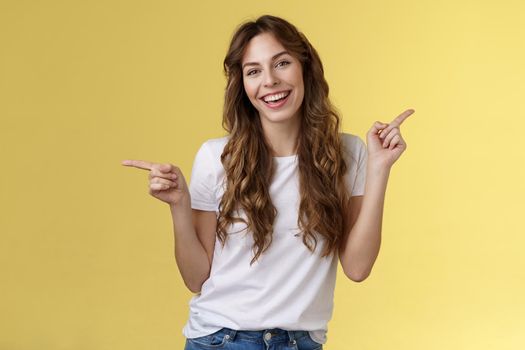 Girl have two suggestions pointing sideways. Cheerful charismatic curly-haired attractive woman pointing left right index fingers introduce promo products smiling broadly lively recommend ad.