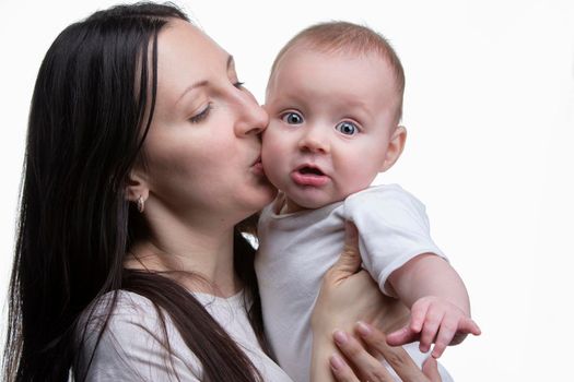 Mom kisses her little son on a light background. Motherhood.