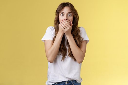 Shocked ambushed speechless cute girl hear impressive rumor shut mouth hold hands lips stare camera astonished eavesdrop juicy stunning conversation stand yellow background. Copy space