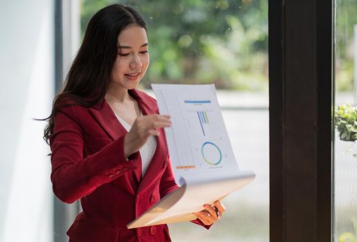 Smiling asian woman standing while checking financial report at office.