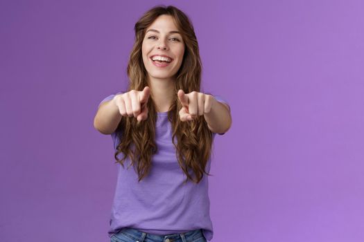 Its you. Friendly glad joyful happy curly-haired girl pointing fingers camera smiling broadly laughing congratulate friend singing song indicating boyfriend make choice stand purple background.