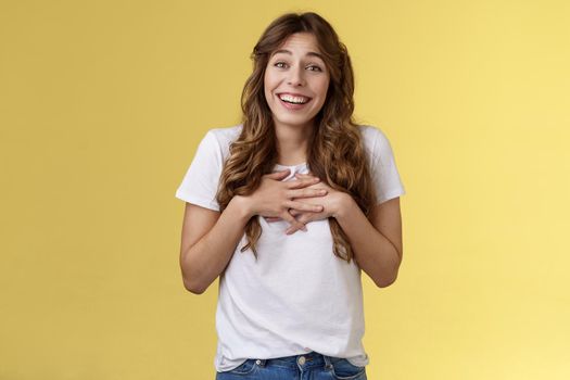 Surprised touched grateful charming caucasian curly-haired female appreciate effort thanking awesome gift press hands heart moved lovely nice present smiling broadly thankful yellow background.