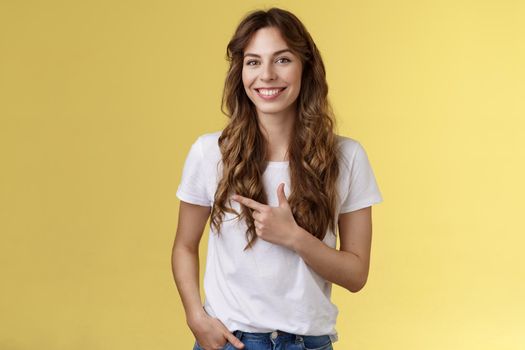 Sassy confident happy charismatic young woman long curly hairstyle hold hand pocket relaxed outgoing expression pointing left index finger inviting local cafe discuss friend favorite places. Lifestyle.