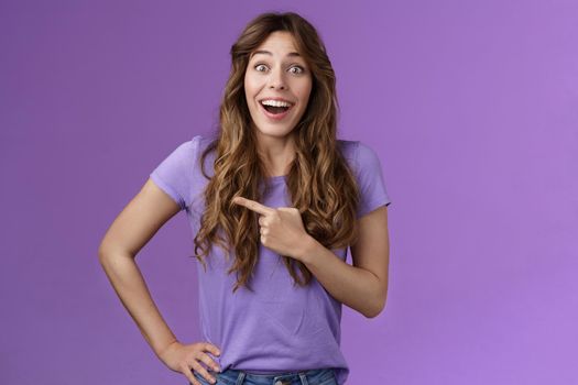 Lively excited enthuasitic good-looking woman curly hairstyle open mouth fascinated look admiration joy share awesome place location pointing left smiling broaldy thrilled purple background.