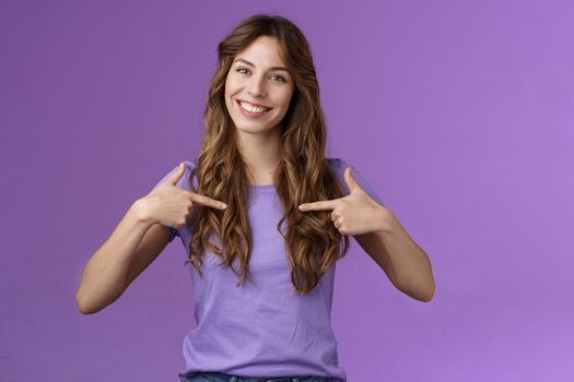 Cheerful motivated professional assertive curly woman pointing herself center smiling broadly propose own help wanna participate boastful talking accomplishments stand purple background.