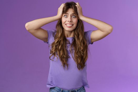 Girl feel panic troublesome perplexed situation clench teeth intense stare camera grab head distressed upset going insane crazy pissed popping eyes feel rage disappointment stand purple background. Lifestyle.