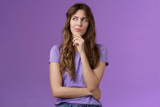 Girl trying solve problem thinking solution make hmm face smirk frowning thoughtful look away touch chin pondering making choice deciding how act what do stand purple background focused. Lifestyle.