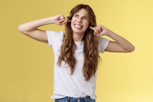 Angry displeased annoyed curly-haired beautiful girl grimacing make wry face stare up irritated noise comming from neighbours above clench teeth plug index fingers ears hate loud music playing. Lifestyle.