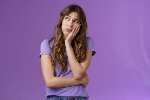 Troubled bored sad european girl long curly brown hair lean palm look up indifferent sighing lonely dying boredom home alone nothing do thinking regret missed party stand purple background. Lifestyle.