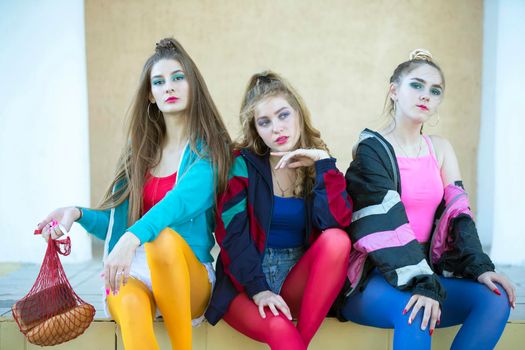 Three pretty girls dressed in the style of the nineties are sitting on the steps.
