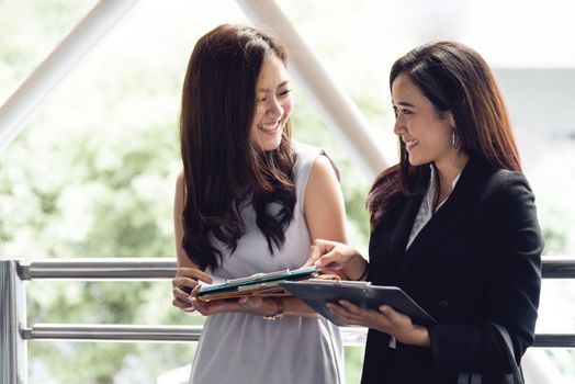 Two happy young Asian businesswomen looking into document file folder for analyzing profit or sale break even point after marketing. Business teamwork employees of lifestyle working women concept.