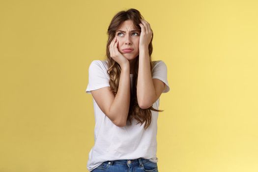 Shocked timid insecure young panicking woman wanna cry standing anxious frightened grab head both hands freak out look away praying for help terrified stand yellow background horrified. Lifestyle.