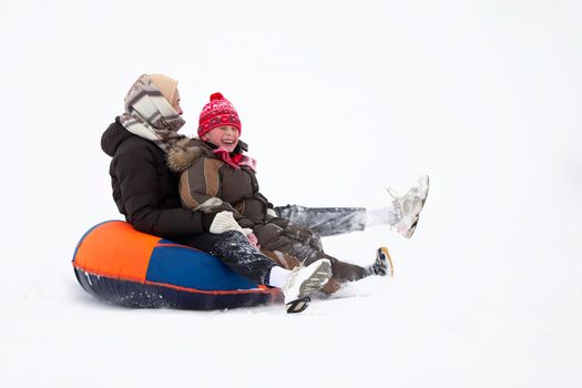 Winter entertainment. Cheerful people in warm clothes are riding down a snowy mountain on a sled.
